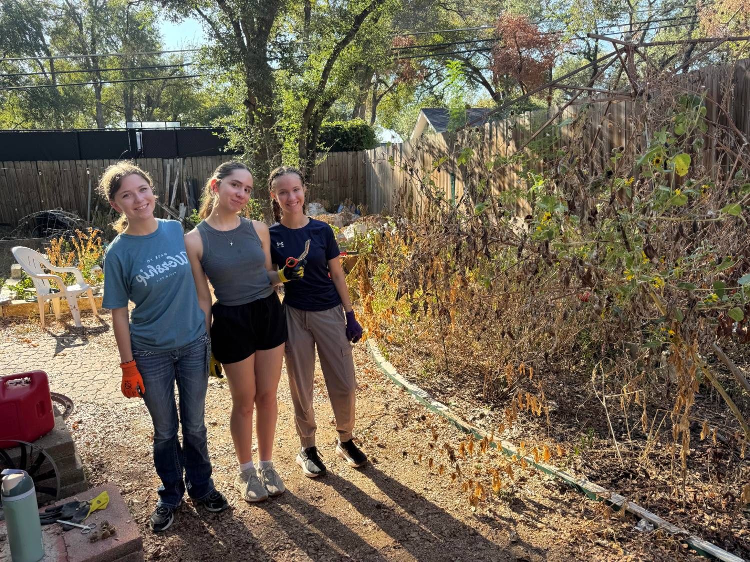 Three SHIFT members in work gloves beside the overgrown section of the garden they cleared